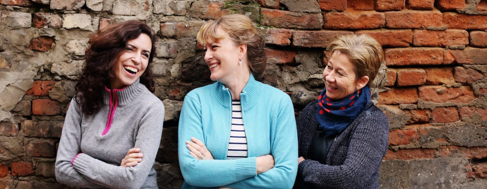 three smiling middle aged women standing by brick wall